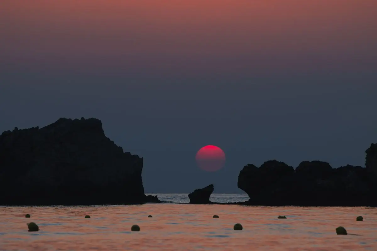 Ο ήλιος δύει ανάμεσα σε βράχους στη θάλασσα