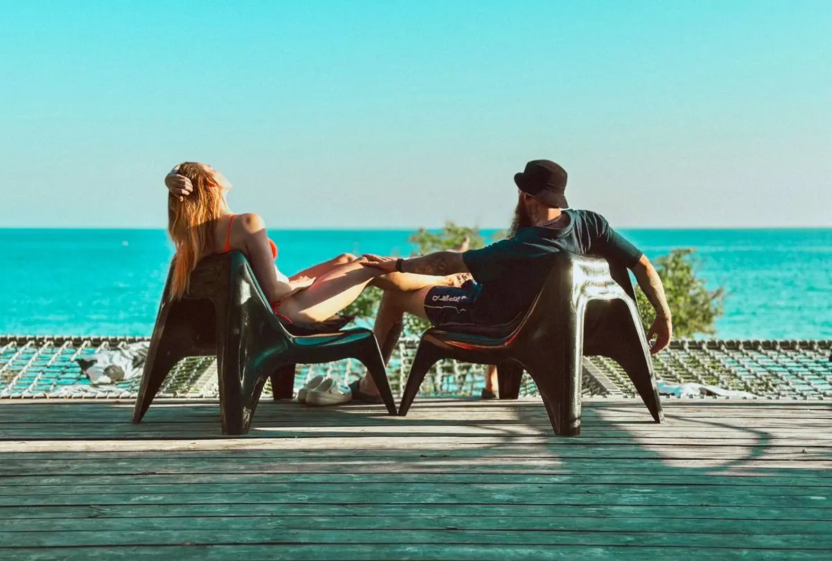 Δύο ξαπλώστρες σε ξύλινη βεράντα, μπροστά σε τιρκουάζ θάλασσα