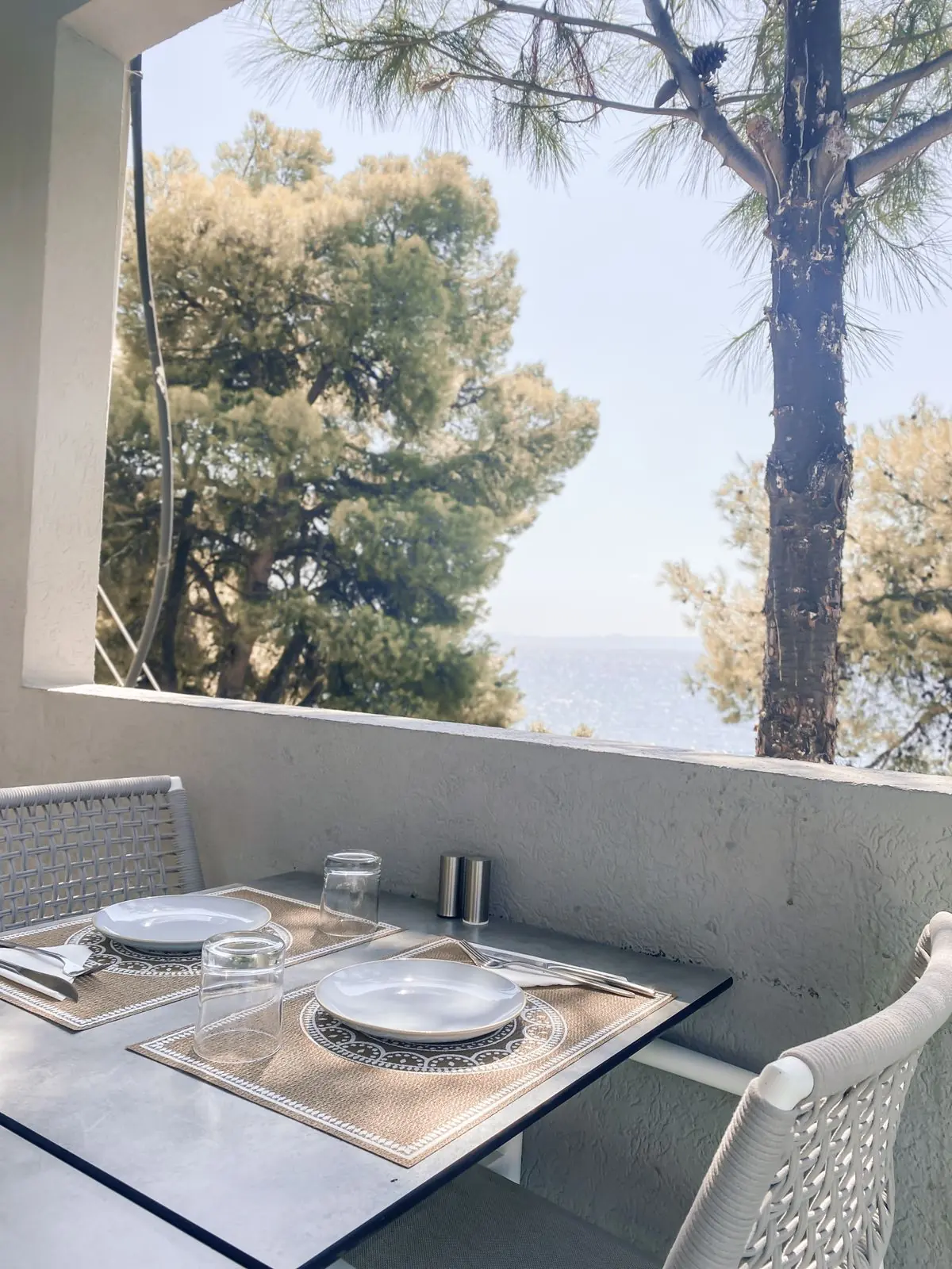 Στρωμένο τραπέζι στο μπαλκόνι, ανάμεσα στα πεύκα και τη θάλασσα
